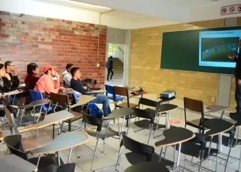 Aula universitaria semivacía con un profesor de pie frente a los pupitres