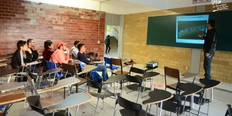 Aula universitaria semivacía con un profesor de pie frente a los pupitres